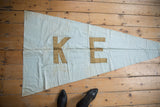 Upper corner of the vintage K E banner in faded light blue fabric, with soft creases.