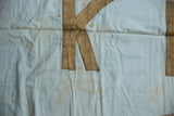 Gold sewn 'K' on light blue vintage banner, with aged discoloration.