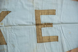 Golden-brown letter 'E' detail on light blue banner, showing fabric creases and patina.