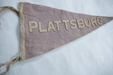 Vintage Plattsburg felt pennant showing aged texture, beige binding, and braided ties.