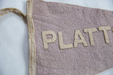 Vintage Plattsburg felt banner showing aged texture, beige 'PLATT' lettering, and sewn edge with ties.