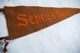 Angled view of the antique brown felt pennant, highlighting its hand-sewn orange lettering.