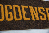 A close-up of the stitched gold felt lettering on the antique brown wool banner.