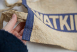 Hand holding antique felt pennant, showing aged beige wool, blue stripe, and stitching.