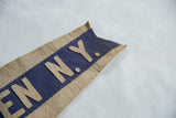 Aged beige felt letters 'N.Y.' hand-sewn on blue felt with textured border.