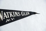 Close-up of black felt pennant showing white 'Watkins Glen N.Y.' lettering and texture.