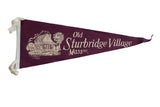 A vintage burgundy felt pennant for Old Sturbridge Village showing a cottage with a water wheel.