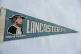 Vintage teal felt pennant with Amish man graphic, white text, and aged patina.