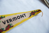 Curved tip of vintage Vermont felt pennant, showing yellow border and red pinecones.