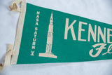 Teal green felt pennant's left side showing 'NASA SATURN V' text and aged cream binding.
