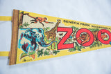 Angled view of vintage Seneca Park Zoo pennant featuring retro elephant, giraffe, monkey graphics.