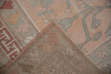 Folded corner of distressed Oushak carpet, revealing worn rose and sage patterned pile with visible woven foundation.