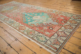 Distressed vintage Oushak runner: worn coral field, turquoise medallion, ivory floral border.
