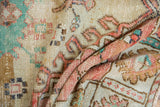 Folded distressed Oushak rug showing faded floral motifs, soft red, turquoise, and ivory pile.