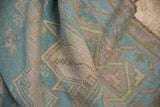 Supple hand-woven texture of a folded Soumak rug in beige, pale denim blue, and mauve.