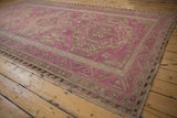 Angled view of a vintage Soumac rug with a distressed fuchsia field and sand geometric medallions.