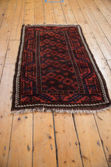 Antique Belouch rug corner, ivory selvage, geometric field in madder and navy, tattered fringe.