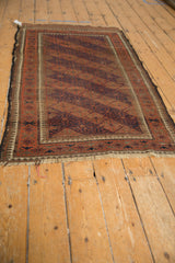 Angled view of a vintage Belouch rug, highlighting worn pile, tattered ends, and pawn motif borders.