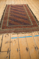 Worn Persian Belouch rug showing navy and chestnut guls, pawn border, tattered edge.