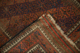 Vintage Belouch rug corner shows chocolate, navy geometric guls, tattered fringe, and striped back.