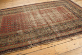 Antique Serbend rug end with tattered fringe, showing madder red field, boteh, meandering vine, and pawn motif borders, with wear.