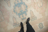 Distressed vintage Oushak carpet, ivory field with faded pink and pale blue geometric motifs.
