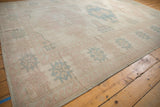 Distressed Oushak rug section: worn texture, geometric floral buds, dusty pink, pale blue.