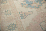 Distressed Oushak carpet's faded geometric pattern in ivory, dusty pink, and pale denim blue.
