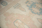Geometric dusty pink and pale denim blue motifs on a distressed ivory vintage Oushak rug.
