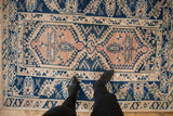 Distressed texture of a vintage Melas rug, showing geometric cobalt blue motifs on beige.