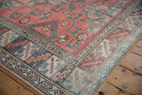 Distressed Melas carpet corner, featuring geometric motifs in dusty red and sky blue.