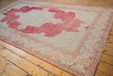 Distressed Oushak rug corner with faded cherry red scrolling spandrels and geometric borders.