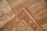 Folded corner of vintage distressed Kars carpet, showing pale brown pile and pink-toned border motifs.