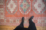 Distressed vintage Oushak rug showcasing geometric floral blossom borders in soft cinnabar red and blue.