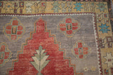 Vintage distressed Oushak rug close-up: dusty cherry red stepped medallion, stylized floral motifs, and aged texture.