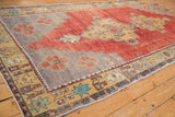 Corner of vintage distressed Oushak rug with geometric saffron border and faded cherry red field.
