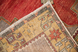 Corner detail of distressed Oushak carpet with dusty red field, saffron geometric starburst border, and corded edge.
