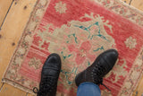 Distressed vintage Oushak rug with abrashed red, turquoise, beige motifs, showing wear underfoot.