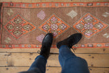 Distressed vintage Kars rug with a tangerine diamond, mauve and ivory floral details.