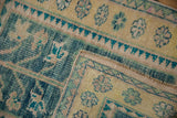 Distressed Oushak rug fold, revealing worn saffron pile and turquoise zig-zag border.
