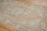 Distressed Oushak rug displaying Rococo scrolling motifs in faded sandalwood and seafoam.