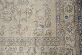 Corner view of distressed vintage Sparta rug, showing faded ivory vinery and dusty blue border.