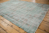 Distressed vintage Oushak carpet showing worn jade green and ivory floral motifs.