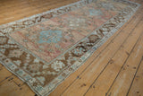 Textured distressed Oushak runner showing geometric brown border and abrashed rose field.