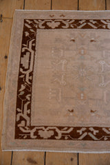 Distressed Oushak rug corner, featuring deep chocolate bronze arabesque border and faded ivory field.