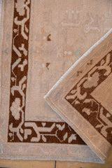 Distressed Oushak rug border featuring chocolate arabesque design and worn ivory field.