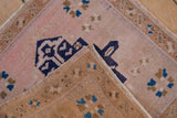 Folded distressed Turkish Oushak rug, showing blush pile, navy geometric motifs, and beige side cord.