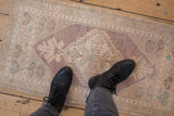 Distressed Oushak mat runner featuring diamond medallion, faded floral patterns, and an abrashed lavender ground.
