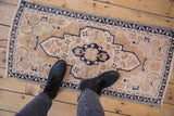 Distressed Oushak rug corner with meandering cobalt blue vine border on beige floral field.