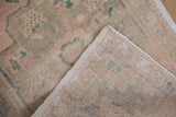 Folded distressed Oushak rug showing ivory pile, visible foundation, and intact side selvage.